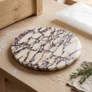 May include: A circular marble serving board featuring a polished surface with a distinct white base and deep purple veining throughout. The stone slab has a smooth, flat top and straight edges, showcasing natural patterns in the mineral composition.
