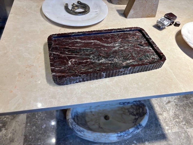 May include: A rectangular tray crafted from deep red and dark green marble with prominent white veining. The tray features a raised, fluted edge design that runs along the entire perimeter, providing a textured border to the polished surface.