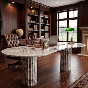 May include: A large oval desk with a white and grey marble top supported by two fluted marble columns. The desk holds a laptop, a small analog clock, and a pen stand. A green banker lamp sits on the desk, which is placed in a room with wood shelves.
