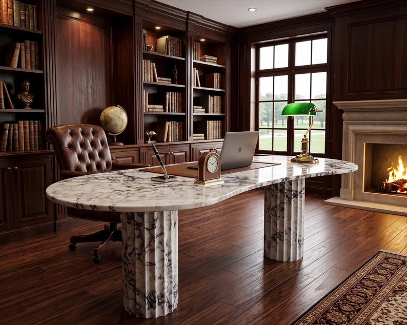 May include: A large oval desk with a white and grey marble top supported by two fluted marble columns. The desk holds a laptop, a small analog clock, and a pen stand. A green banker lamp sits on the desk, which is placed in a room with wood shelves.