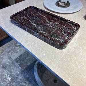 May include: A rectangular tray featuring a deep red and black marbled pattern with white veining. The tray has a distinctively ribbed or fluted texture along its outer vertical edges, creating a structured and consistent appearance throughout the piece.
