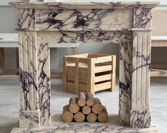 May include: A fireplace mantel constructed from white marble with prominent dark purple veining. The structure features a rectangular top shelf, two vertical fluted columns on either side, and a base. A small stack of round wooden logs sits inside.
