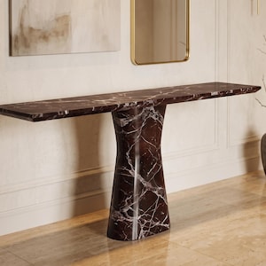 May include: A long, narrow console table crafted from dark brown marble with prominent white veining. The table features a flat, rectangular top supported by a single, wide, pedestal-style base that tapers slightly toward the center.