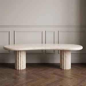 May include: A beige travertine console table with an elongated, kidney-shaped top and two thick, cylindrical, fluted pedestal bases. The stone surface features natural porous textures and variations in color throughout the entire structure.