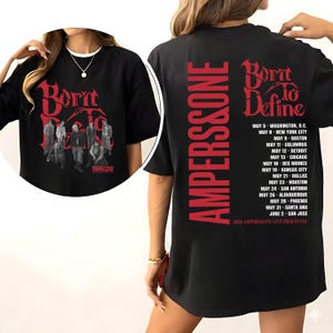 May include: A black short-sleeve t-shirt featuring red graphic text and imagery. The front displays the text Born To Define with a group of people. The back features the text AMPERS&ONE, Born To Define, and a list of tour dates in the USA.