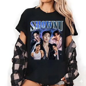 May include: A black short-sleeved t-shirt featuring a graphic print of five individuals. The text SHOWNU is printed in a metallic blue font above the group. The background of the graphic shows a blue lightning effect. The shirt is worn with a black and white plaid shirt.