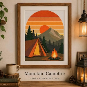 Könnte beinhalten: Ein gerahmtes Kreuzstichmuster mit dem Titel Mountain Campfire, das ein Zelt, ein Lagerfeuer, Tannen und ein Gebirge unter einem Sonnenuntergangshimmel mit orangefarbenen und gelben horizontalen Streifen zeigt.