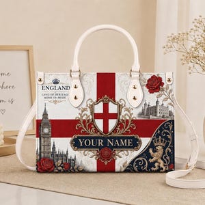 Könnte beinhalten: Eine rechteckige Handtasche mit der englischen Flagge, einem zentralen Wappen und dem Schriftzug "YOUR NAME". Das Design zeigt Big Ben, den Tower of London, einen Löwen und rote Rosen. Sie hat weiße Griffe und einen abnehmbaren Schulterriemen.