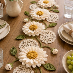 May include: A crochet table runner featuring four large white daisy flowers with yellow centers, interspersed with small white crochet doilies, green leaves, and small white flower buds, arranged in a vine-like pattern along the center.