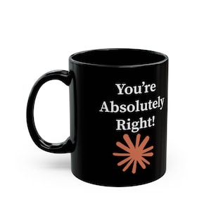 Peut inclure: Une tasse en céramique noire avec une anse incurvée, présentant le texte blanc "You're Absolutely Right!" imprimé sur le devant, placé au-dessus d'un motif graphique en forme d'étoile orange à plusieurs branches sur le côté du récipient.