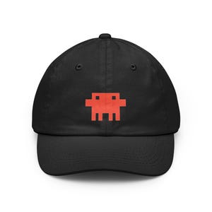 Peut inclure: Une casquette de baseball noire ornée d'un motif d'extraterrestre rouge pixélisé centré. La casquette présente une calotte structurée, une visière incurvée et des œillets brodés sur les panneaux supérieurs. Le design est simple et contrasté.