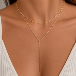 Peut inclure: Un collier superposé doré composé de deux chaînes délicates. La chaîne supérieure est un brin simple, tandis que la chaîne inférieure forme une chute en Y. Les deux chaînes sont ornées de petites perles dorées espacées régulièrement.