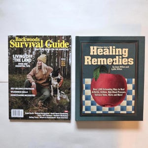 May include: A Backwoods Survival Guide magazine featuring a person and dog in a forest, alongside a hardcover book titled Bottom Line's Healing Remedies by Joan Wilen and Lydia Wilen, which displays a large red apple over a blue and white checkered pattern.