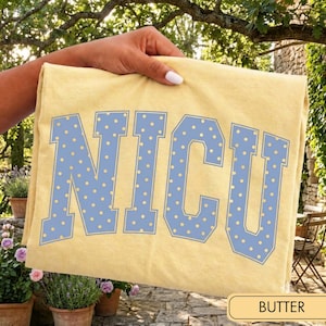 May include: A pale yellow t-shirt featuring the letters NICU in a large, collegiate-style font. The letters are light blue with a repeating pattern of small yellow dots and a thin light blue outline, centered on the front of the garment.