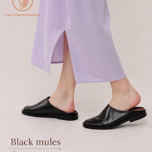 May include: Black mules made of soft genuine leather with a flat sole and a square toe design. The footwear is shown paired with a light purple garment featuring a side slit. The image includes the text PAVLINASHOESUA and Black mules.