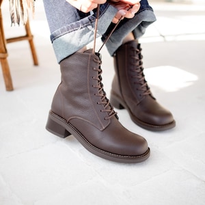 May include: A pair of dark brown leather lace-up boots with a pebbled texture, featuring a rounded toe, a low block heel, and matching brown laces. The boots have a side zipper closure and a sturdy sole, providing a classic look for everyday wear.
