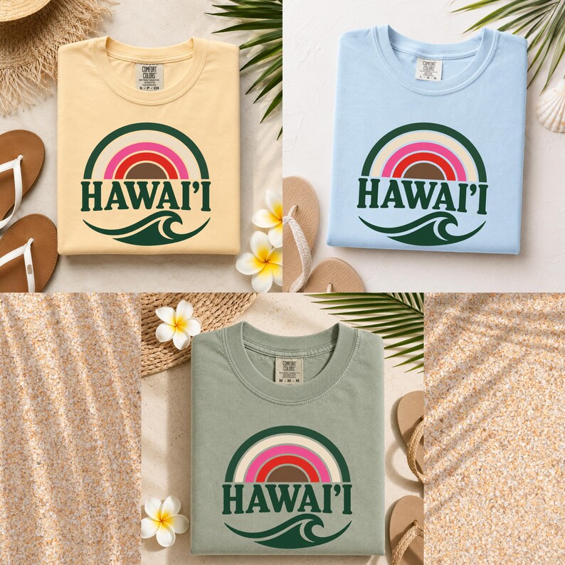 May include: Three crew neck t-shirts in light yellow, light blue, and sage green. Each shirt features a graphic of a multi-colored rainbow arching over the text HAWAI'I and a dark green ocean wave. The shirts have a Comfort Colors brand label.