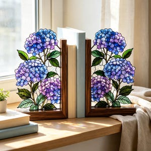 以下が含まれることがあります： 青と紫の紫陽花の房と緑の葉が描かれたステンドグラスパネルを備えたL字型のブックエンドのペア。ダークブラウンの木製ベースにセットされており、複雑な鉛線と鮮やかな花のディテールが施されています。