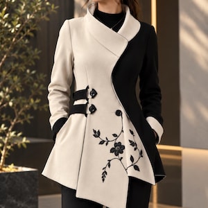 May include: A two-tone jacket featuring a cream-colored right side and a black left side. The jacket has a high collar, long sleeves with black cuffs, and two black side straps with buttons. Black floral embroidery adorns the cream front panel.
