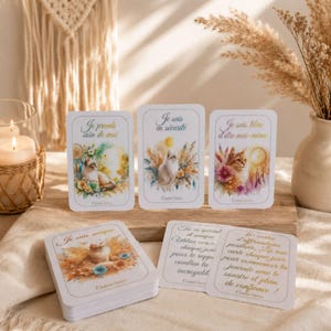 Könnte beinhalten: Ein Set rechteckiger Affirmationskarten mit Aquarellillustrationen von Katzen, umgeben von Blumen und Traumfängern. Die Karten zeigen französischen Text wie Je prends soin de moi, Je suis en sécurité und Je suis libre d'être moi-même, mit goldfarbenen Rändern und weichen, pastellfarbenen künstlerischen Designs.