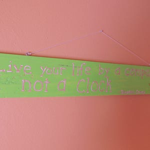 Puede incluir: Un letrero de madera verde con texto blanco que dice "Live your life by a compass not a clock - Stephen Covey". El letrero tiene un diseño de rosa de los vientos en la esquina inferior derecha.