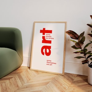 May include: A rectangular framed wall art print featuring the word art in large red letters. The text reads some people are artists above the word art and some themselves are art below it. The frame is light wood and the background is white.