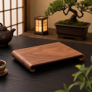 May include: A rectangular wooden display stand with a smooth, polished brown surface and curved, scroll-like edges on the short sides. The stand features a visible natural wood grain pattern and is elevated slightly above the surface by its curved ends.