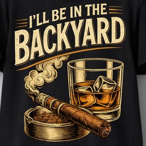 May include: A black t-shirt featuring a graphic print with the text I'LL BE IN THE BACKYARD in beige. The design includes a brown cigar resting on a round ashtray with rising smoke, positioned next to a glass of amber liquid with ice cubes.