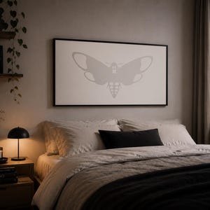 May include: A rectangular wall art piece featuring a light grey moth silhouette centred on a white background, enclosed in a thin black frame. The moth design displays symmetrical wings and a detailed abdomen, presented as a minimalist graphic print.