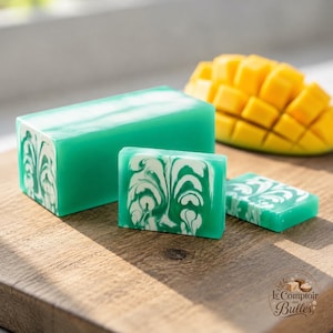 Peut inclure: Un bloc rectangulaire de savon bleu sarcelle avec un motif tourbillonnant blanc marbré, une tranche de savon rectangulaire assortie plus petite et un fruit mangue jaune coupé en dés. Le savon présente une finition lisse et semi-translucide.