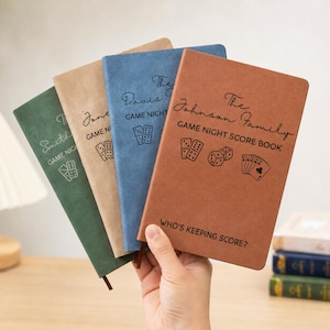 May include: Four rectangular score books in green, tan, blue, and brown with a soft-touch finish. Each cover features custom family names, the text GAME NIGHT SCORE BOOK, icons of dominoes, dice, and playing cards, and the text WHO'S KEEPING SCORE?