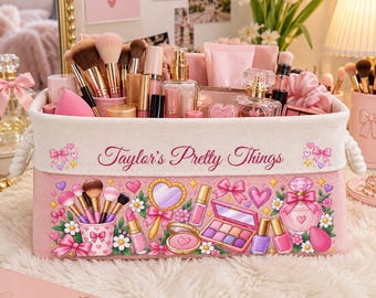 Puede incluir: Una caja de almacenamiento rectangular de tela rosa con asas de cuerda, que presenta el texto Taylor's Pretty Things y un estampado gráfico colorido de brochas de maquillaje, perfume y polveras. La caja contiene brochas y frascos.