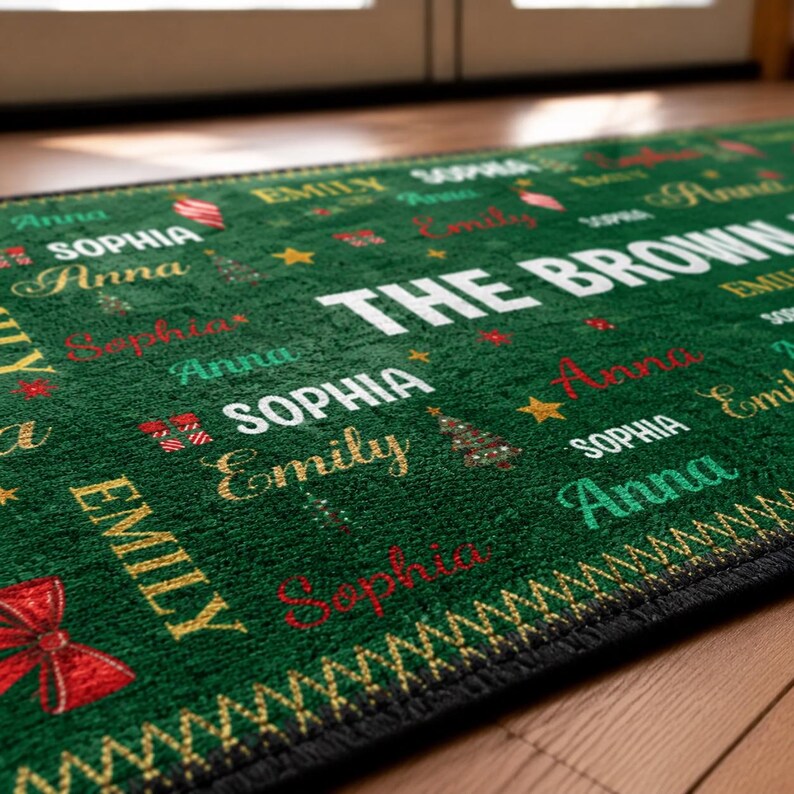 Puede incluir: Un felpudo rectangular verde con el texto blanco THE BROWNS y nombres repetidos como Anna, Sophia y Emily en varias fuentes y colores. La alfombra est&aacute; decorada con peque&ntilde;os &aacute;rboles de Navidad, estrellas y lazos rojos.
