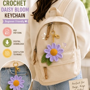 May include: A crochet daisy keychain featuring a purple flower with a yellow center and two green leaves attached to a gold-tone metal ring. The text reads NovaBlossomStudio, CROCHET DAISY BLOOM KEYCHAIN, Beginner Friendly, PDF PATTERN, DIGITAL DOWNLOAD, EASY & FUN TO MAKE, and Perfect for Bags, Keys & Gifts!