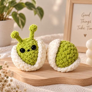 Peut inclure: Deux petites créatures rondes en crochet faites à la main en fil vert citron, chacune nichée dans une coquille en crochet blanc texturé. La créature de gauche possède deux antennes et deux grands yeux noirs brillants, celle de droite est une sphère verte.