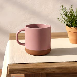 Peut inclure: Une tasse en céramique avec une partie supérieure rose mate et lisse, contrastant avec une base en terre cuite non émaillée. La tasse présente une anse arrondie sur le côté gauche et un corps cylindrique au design épuré et fonctionnel.