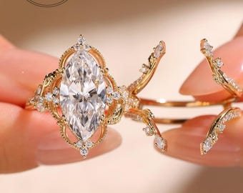 May include: A gold ring set featuring a large marquise-cut center stone surrounded by a decorative filigree frame with small accent stones. The set includes a matching open-style band with branch-like details adorned with tiny clear stones.