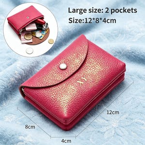 May include: A hot pink textured wallet with a snap button closure and the letters XY embossed on the front. The wallet features two pockets and measures 12 by 8 by 4 centimeters. An inset shows the wallet open, containing coins, cards, and keys.