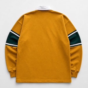 May include: A long-sleeve rugby shirt in mustard yellow featuring a white collar and horizontal dark green bands on the sleeves, accented by thin white stripes bordering the green sections, with ribbed cuffs and a straight hemline.