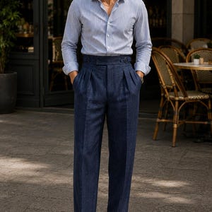 May include: A light blue and white vertical striped long-sleeve button-down shirt paired with high-waisted dark navy blue trousers featuring double pleats, a side-adjuster waistband, and cuffed hems, worn with dark brown leather loafers.