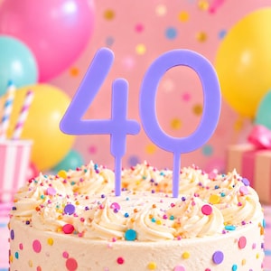 Könnte beinhalten: Ein hellvioletter Tortenstecker in Form der Zahl 40 mit zwei dünnen Stielen zum Einstecken. Der Tortenstecker steht aufrecht auf einer runden Torte, die mit weißem Zuckerguss und bunten, runden Streuseln verziert ist.