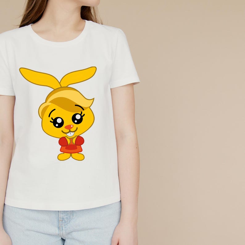 May include: A white short-sleeved t-shirt featuring a centered graphic of a yellow cartoon rabbit with large black eyes, long ears, and a small red shirt. The rabbit has a small orange nose and two visible white front teeth, standing upright.