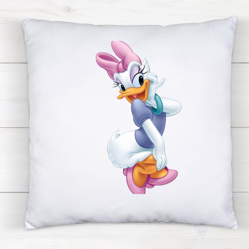 May include: A square white throw pillow featuring a centered, full-color graphic illustration of Daisy Duck. The character is depicted with a pink bow, a purple shirt, and teal bracelets, standing in a pose with one hand raised to her cheek.