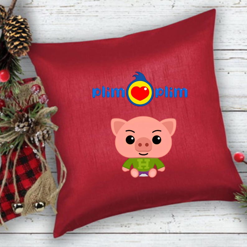 May include: A square red throw pillow featuring the blue text plim plim with a yellow circle and red heart logo above a cartoon pig character wearing a green shirt with a letter H on the front, centered on the fabric surface.