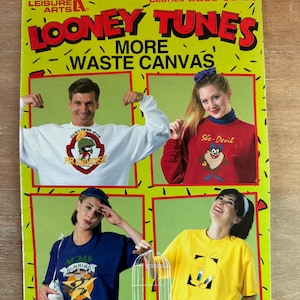 May include: A Leisure Arts Looney Tunes More Waste Canvas craft leaflet featuring four photos of people wearing sweatshirts and t-shirts with embroidered cartoon characters including Marvin the Martian, Taz, Wile E. Coyote, and Tweety Bird.