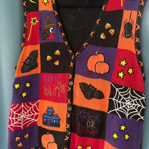 May include: A sleeveless knit vest featuring a patchwork design of black, orange, purple, and red squares. The vest displays embroidered Halloween motifs including pumpkins, bats, spiders, webs, candy corn, stars, moons, and houses with the text Happy Halloween and Trick or Treat.
