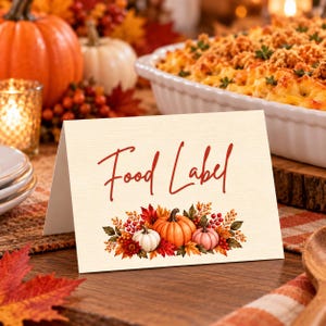 May include: A folded cream-colored card with the text Food Label in red script. Below the text is a watercolor illustration of three pumpkins in orange, white, and pink, surrounded by autumn leaves and red berries on a textured paper surface.