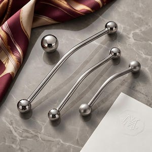 May include: Three polished silver-toned metal cabinet pulls with a curved design and spherical ends. Each handle features a smooth, reflective finish and a consistent arc shape, showcasing a modern hardware aesthetic for furniture or cabinetry.