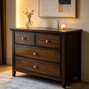 May include: A dark brown wooden dresser featuring two smaller top drawers and two larger bottom drawers, all equipped with round gold-toned knobs. The piece has a rectangular frame with straight legs and a smooth, polished finish on the wood.