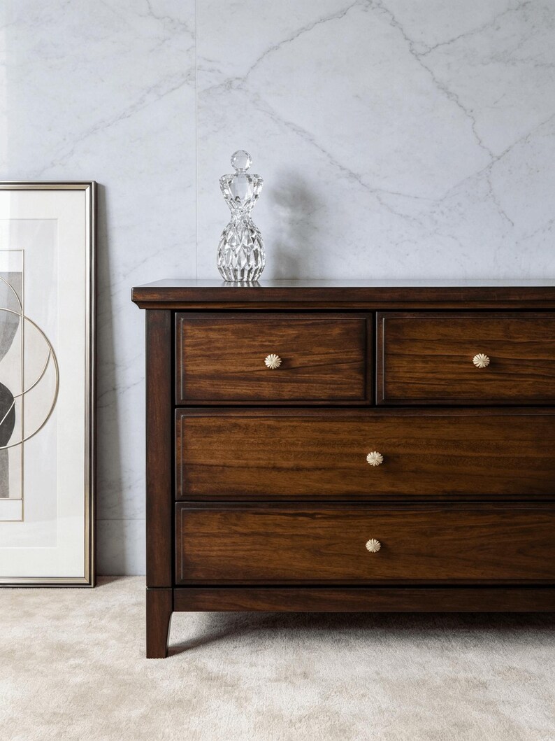May include: A dark brown wooden dresser featuring four drawers with small, round, textured cream-colored knobs. The dresser has a rectangular frame with a smooth top surface and straight legs, showcasing a visible wood grain pattern throughout.